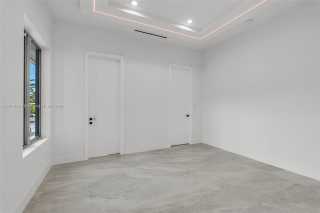 spare room with finished concrete floors, recessed lighting, and a raised ceiling