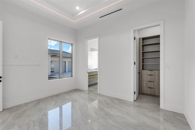 unfurnished bedroom with a tray ceiling, a spacious closet, baseboards, and connected bathroom