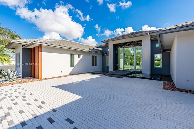 rear view of house with stucco siding, a tiled roof, and a patio