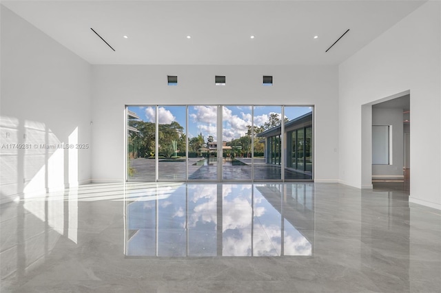 spare room featuring baseboards, marble finish floor, and a towering ceiling