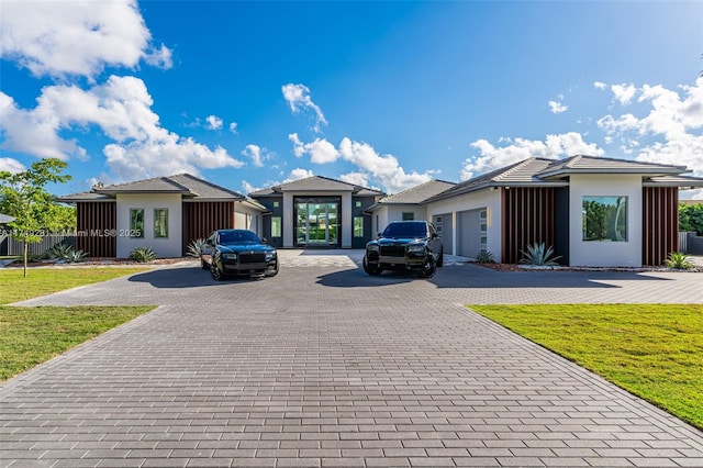 prairie-style home with a garage, stucco siding, decorative driveway, and a front lawn