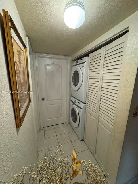 laundry room featuring stacked washer / drying machine, a textured wall, light tile patterned flooring, a textured ceiling, and laundry area