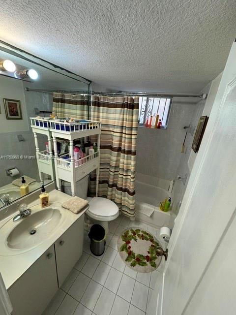 full bath featuring a textured ceiling, toilet, vanity, tile patterned floors, and shower / tub combo with curtain