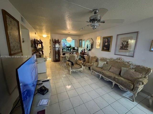 living area with a textured ceiling, light tile patterned flooring, visible vents, and a ceiling fan