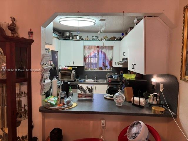 kitchen featuring dark countertops, a toaster, white cabinets, and a sink