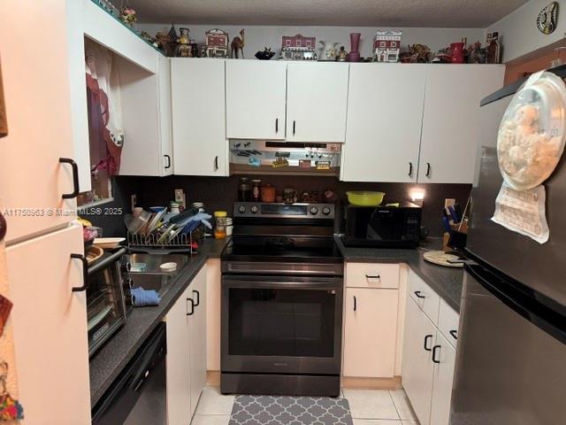 kitchen with dark countertops, white cabinets, light tile patterned flooring, black appliances, and extractor fan