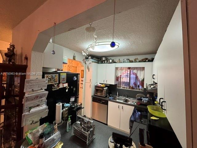 kitchen featuring dark countertops, a textured ceiling, stainless steel dishwasher, white cabinetry, and a sink