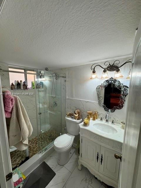 bathroom with a textured ceiling, toilet, vanity, marble finish floor, and a shower stall