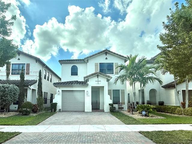 mediterranean / spanish home with a garage, a tiled roof, decorative driveway, and stucco siding