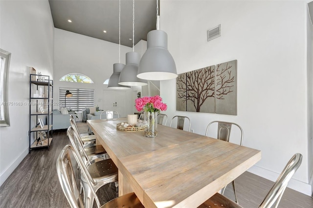 dining space with a towering ceiling, baseboards, visible vents, and wood finished floors