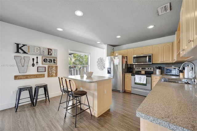 kitchen featuring visible vents, appliances with stainless steel finishes, a kitchen breakfast bar, light brown cabinets, and a sink