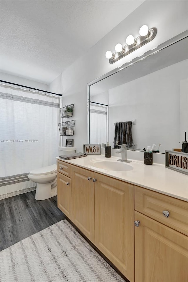 full bath featuring curtained shower, toilet, a textured ceiling, vanity, and wood finished floors