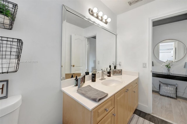 bathroom featuring baseboards, visible vents, toilet, wood finished floors, and vanity