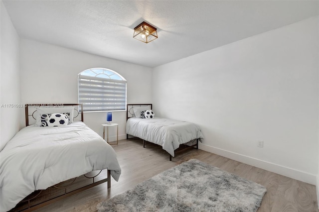 bedroom featuring a textured ceiling, wood finished floors, and baseboards