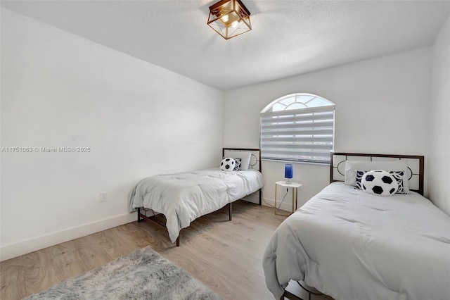 bedroom with a textured ceiling, baseboards, and wood finished floors