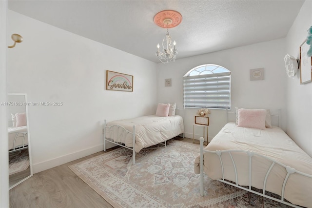 bedroom featuring baseboards, a textured ceiling, an inviting chandelier, and wood finished floors