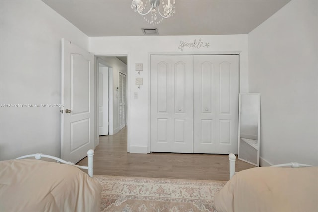 bedroom with baseboards, visible vents, wood finished floors, an inviting chandelier, and a closet