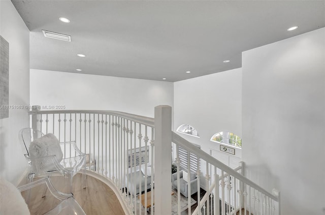 hallway with recessed lighting, visible vents, wood finished floors, and an upstairs landing