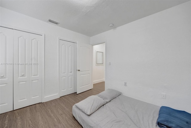 bedroom with a textured ceiling, wood finished floors, visible vents, and multiple closets