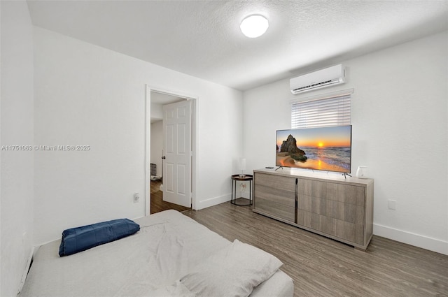 bedroom featuring a textured ceiling, a wall mounted AC, wood finished floors, and baseboards