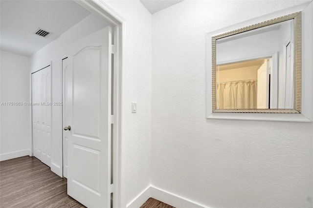 corridor featuring visible vents, baseboards, and wood finished floors