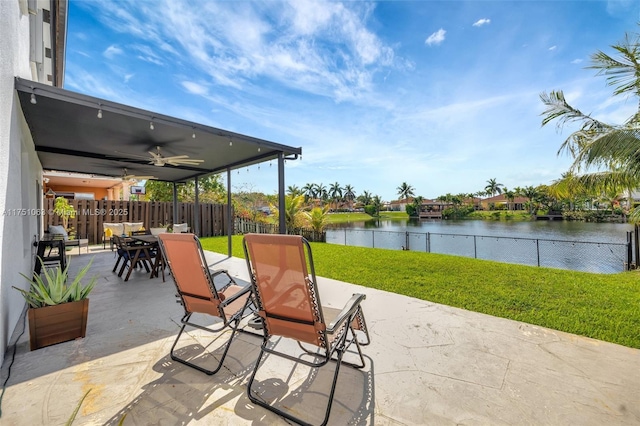 view of patio / terrace with outdoor dining space, a water view, fence, and a ceiling fan