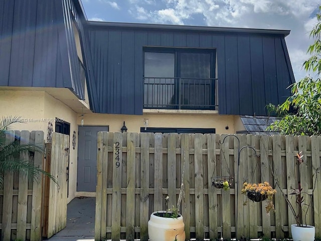 exterior space featuring stucco siding, fence, and mansard roof