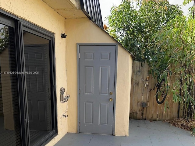 doorway to property featuring fence and stucco siding