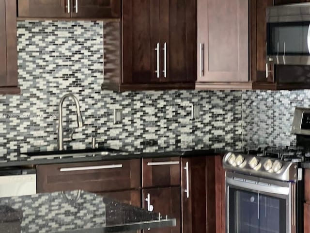 kitchen featuring appliances with stainless steel finishes, a sink, backsplash, and dark stone countertops