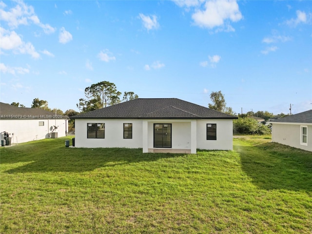 back of house with a shingled roof, a lawn, and stucco siding