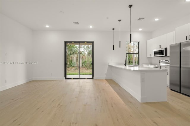 kitchen with white cabinetry, light countertops, appliances with stainless steel finishes, a wealth of natural light, and decorative light fixtures