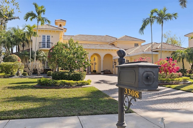 mediterranean / spanish-style house featuring a tiled roof, a balcony, a front lawn, and stucco siding