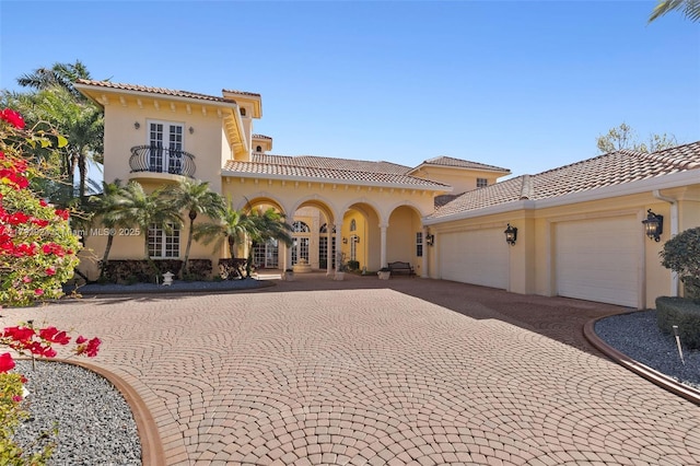 mediterranean / spanish home with a balcony, a tile roof, an attached garage, decorative driveway, and stucco siding