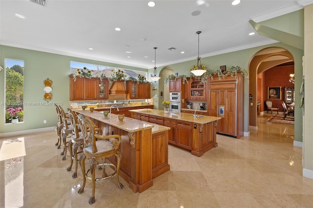 kitchen featuring hanging light fixtures, glass insert cabinets, arched walkways, and a large island with sink