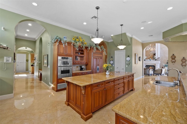 kitchen with brown cabinets, decorative light fixtures, a spacious island, double oven, and a sink