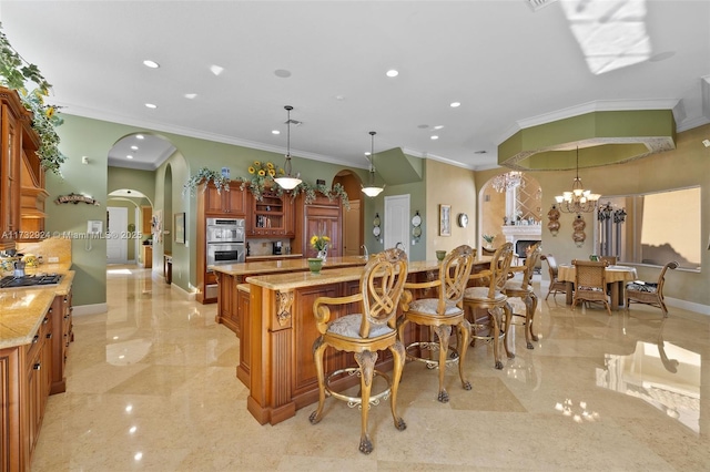 kitchen featuring arched walkways, light stone counters, a center island, hanging light fixtures, and marble finish floor