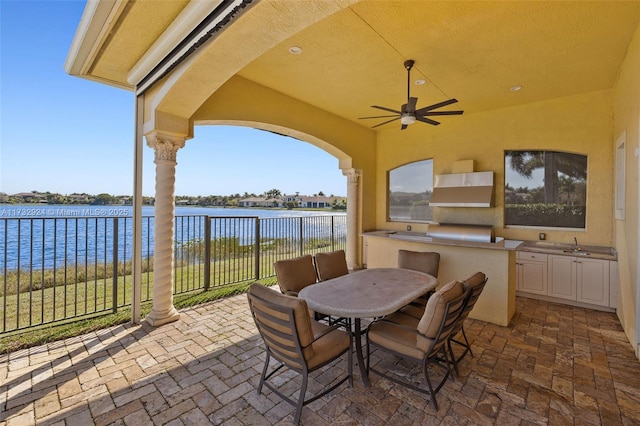 view of patio with ceiling fan, a water view, fence, area for grilling, and outdoor dining space