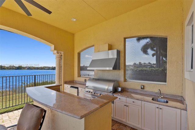 view of patio with area for grilling, a water view, a sink, fence, and exterior kitchen