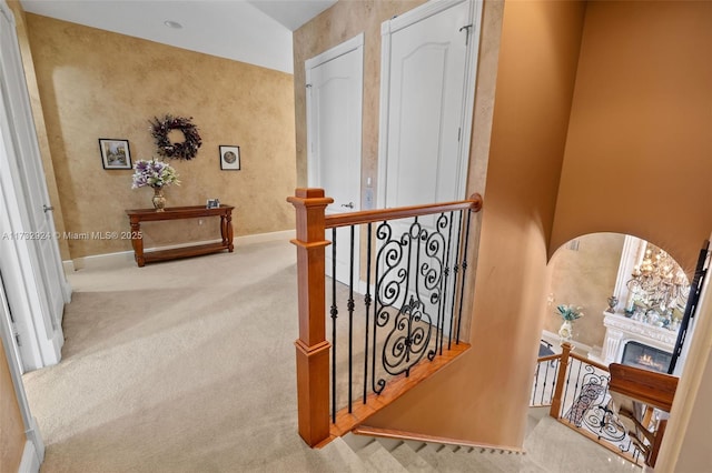 hall featuring arched walkways, baseboards, carpet flooring, and an upstairs landing