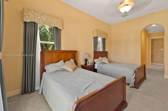 bedroom with baseboards, visible vents, arched walkways, and light colored carpet