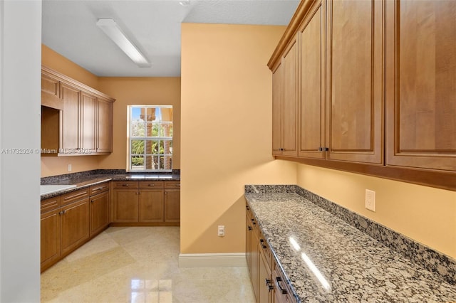 kitchen featuring brown cabinets, baseboards, and dark stone countertops