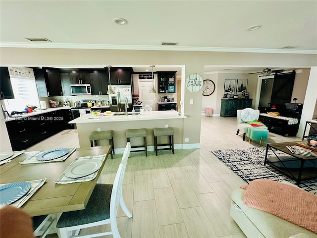 kitchen with visible vents, open floor plan, appliances with stainless steel finishes, dark cabinetry, and crown molding