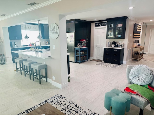 kitchen featuring crown molding, light countertops, dark cabinets, a kitchen bar, and stainless steel refrigerator