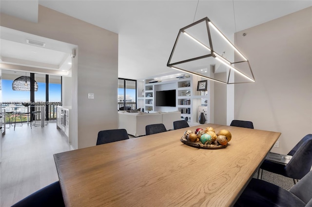 dining space featuring a raised ceiling, wood finished floors, visible vents, and floor to ceiling windows