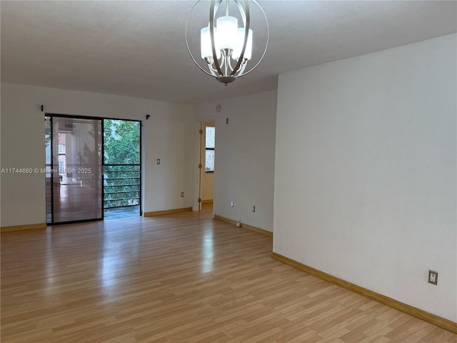 spare room with baseboards, light wood-style flooring, and a notable chandelier