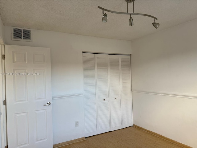 unfurnished bedroom featuring baseboards, visible vents, wood finished floors, a textured ceiling, and a closet