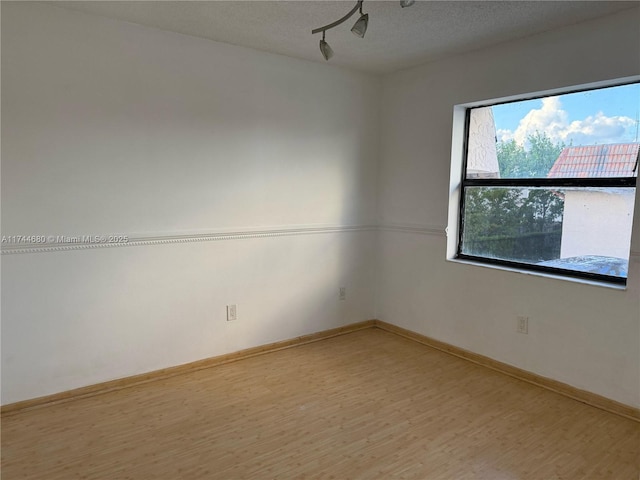 unfurnished room featuring rail lighting, a textured ceiling, baseboards, and wood finished floors