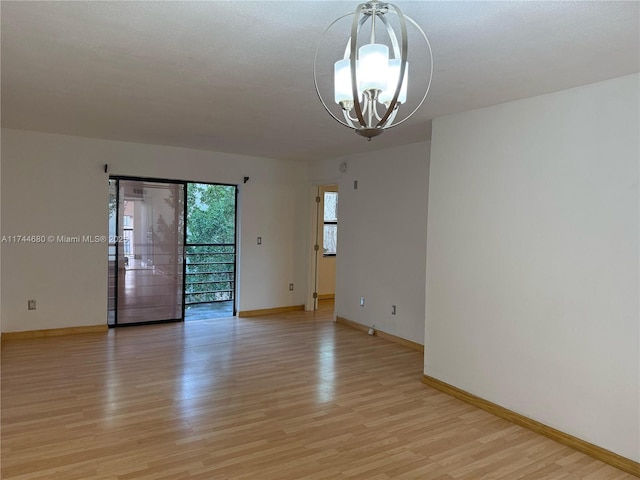 empty room with baseboards, a notable chandelier, and light wood finished floors