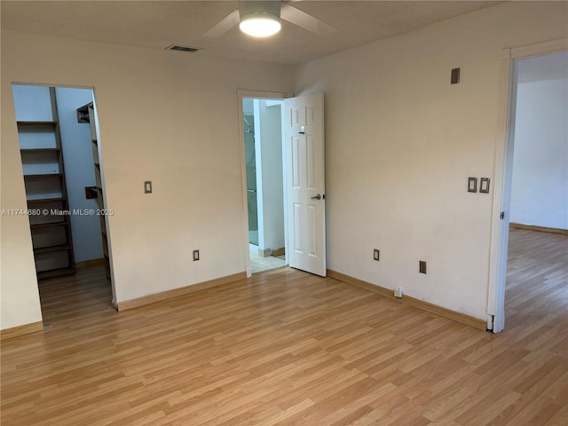 unfurnished bedroom with a spacious closet, light wood finished floors, visible vents, and baseboards