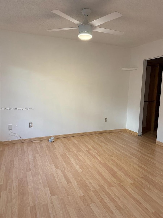 empty room featuring ceiling fan, light wood-style flooring, baseboards, and a textured ceiling